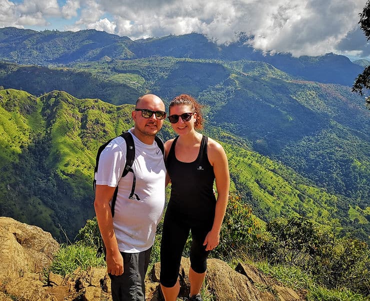 A couple stand on the top of Ella Rock mountain, surrounded by rolling hills covered in thick forest, Sri Lanka