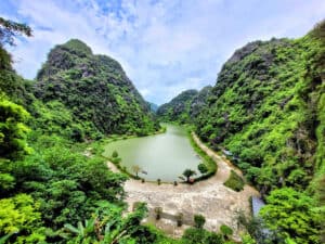 A small green-blue lake sits surrounded by tree-covered mountains in Trang An, Vietnam