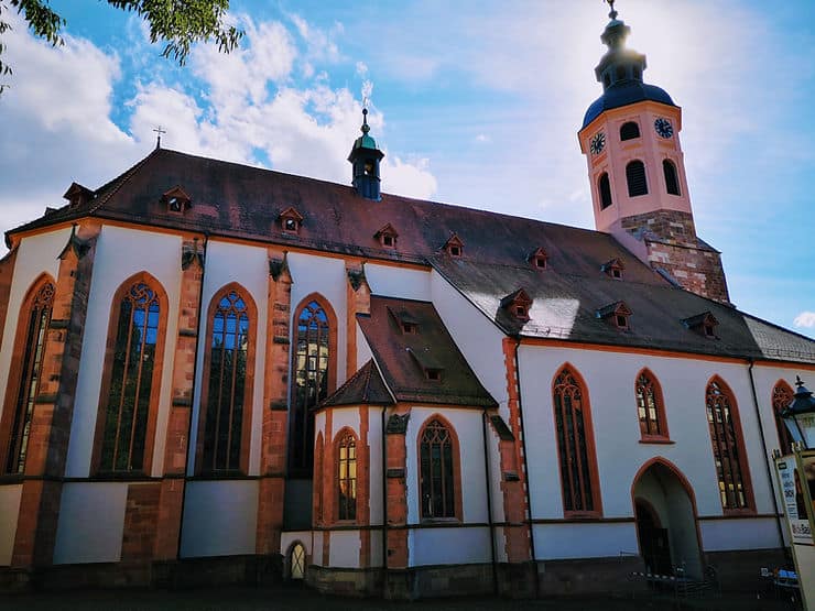 The Collegiate church in Baden-Baden, Germany - a white building with red brick columns, tall glass windows and a small clock tower.