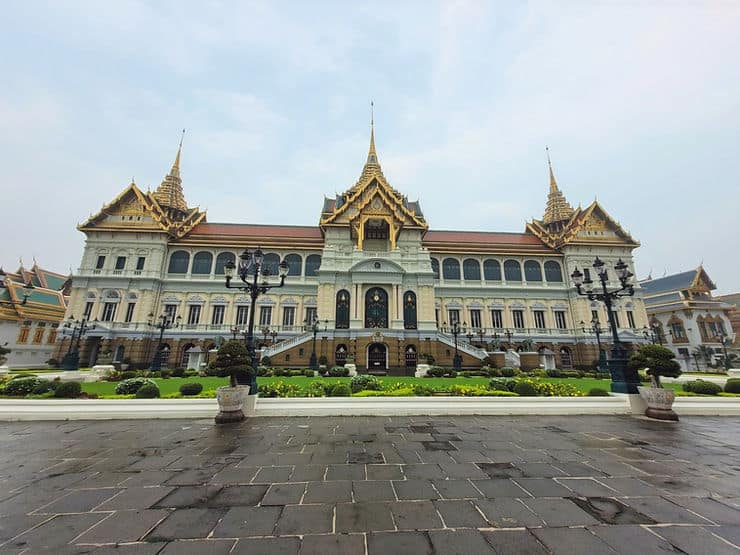 The regal Grand Palace in Bangkok. Its facade is understated, with muted colours of cream and pastel green and three turrets, one to the centre and one at each end of the building. 