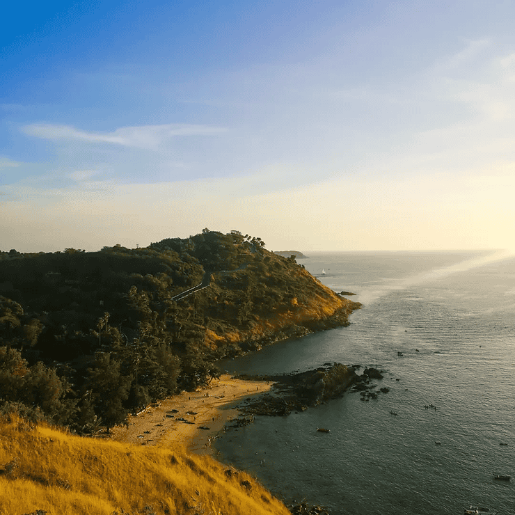 Looking down onto the small sandy cover of Yanui beach, backed by thick green forest and rocky cliffs. The sky is golden as the sun starts to set. 