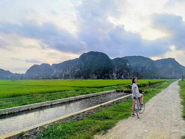 Woman on bicycle surrounded by rice fields and limestone mountains in rural Ninh Binh, Vietnam