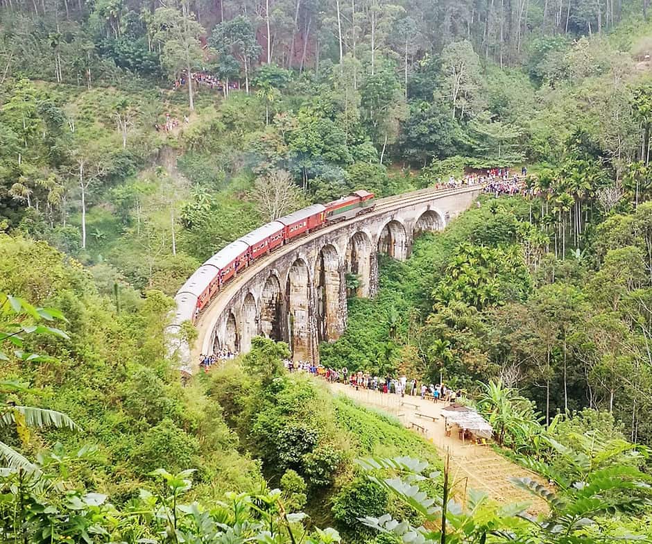 A train passes over the nine arch bridge in Ella, Sri Lanka watched by crowds of onlookers