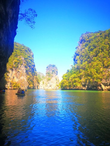 Kayaking in Phang Nga Bay, surrounded by tall limestone islands, covered in trees, appearing from the calm, green-blue water
