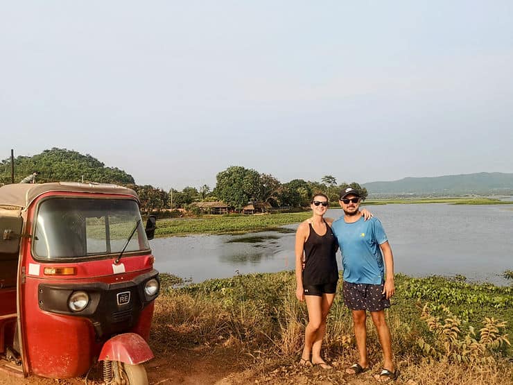 A couple stands by a red tuk-tuk next to a lake in rural Cambodia