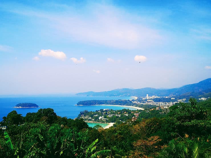 Standing above thick green forest at Karon Viewpoint, looking down to the bright blue sea and golden bays