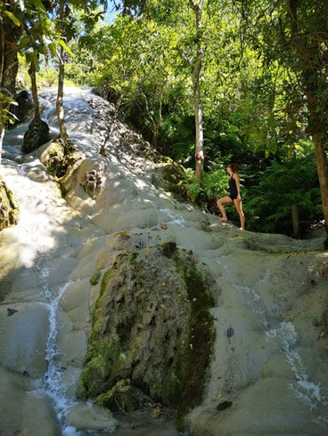 Walking up the Bua Tong waterfalls. Water flows down limestone rocks, surrounded by trees. 