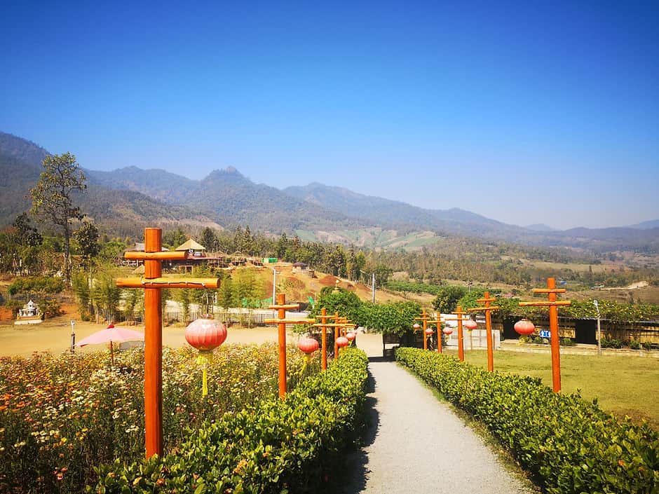 Red wooden poles frame a walkway, surrounded by forest covered mountains in Pai, Northern Thailand.