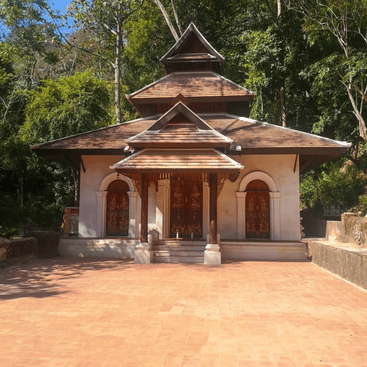 A simple temple building with a pointed roof is nestled in the jungle