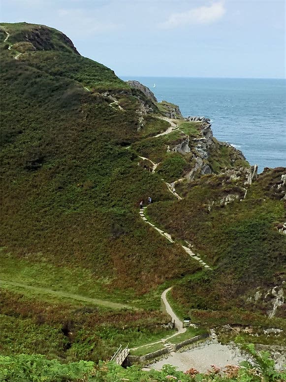 A walking path snakes up a grassy hill with views across the southern coast in North Devon