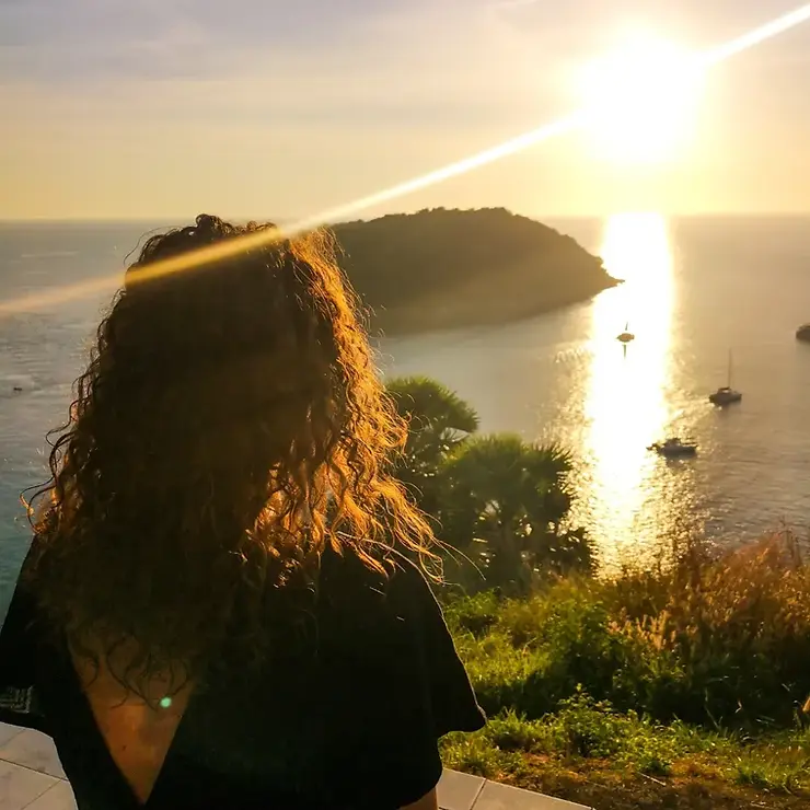 Girl looking out to the sun setting over the ocean at Windmill Viewpoint in Phuket, Thailand
