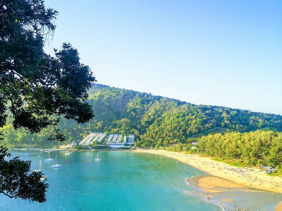 The crystal blue sea and golden sands at Nai Harn beach, Thailand is surrounded by hills of green forests