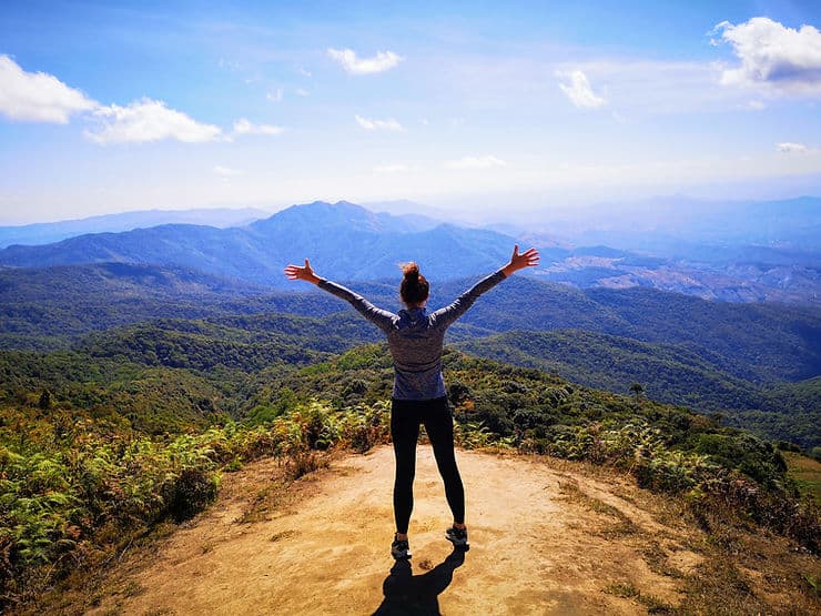 Girl standing with arms in the air looking out across Doi Inthanon National Park, near Chiang Mai, Thailand 