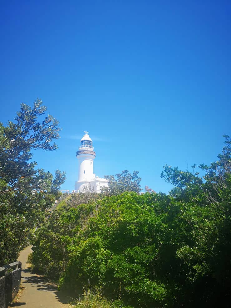 The tree lined path of the Cape Byron walking track skirts the coast as the Cape Byron lighthouse peaks out above the trees. 