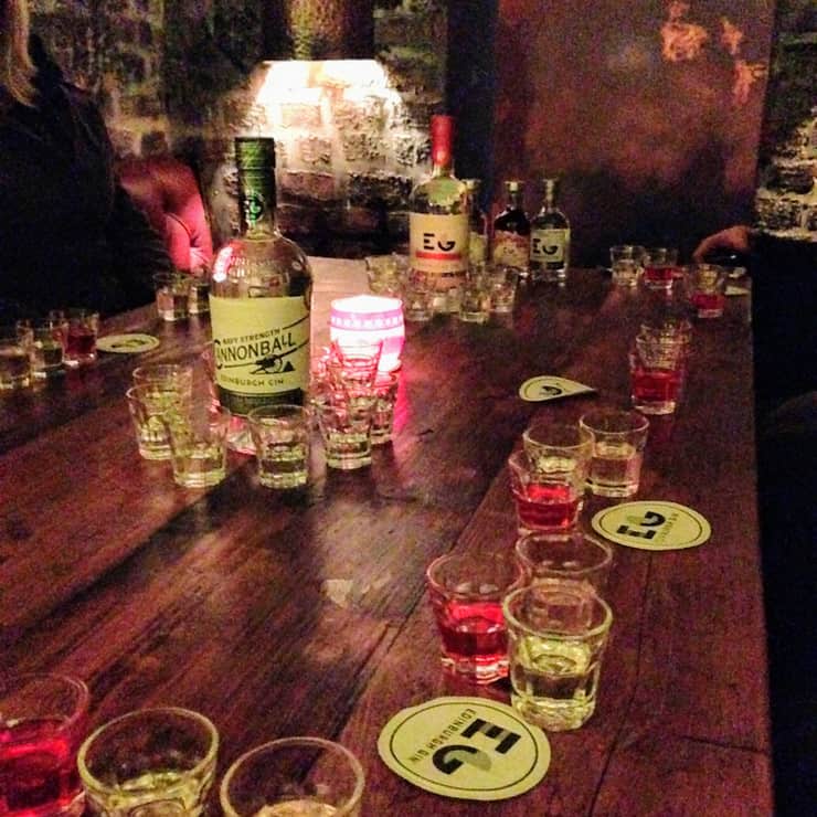 A table is lined up with shot glasses and bottles of gin at a tasting experience at Edinburgh Gin Distillery