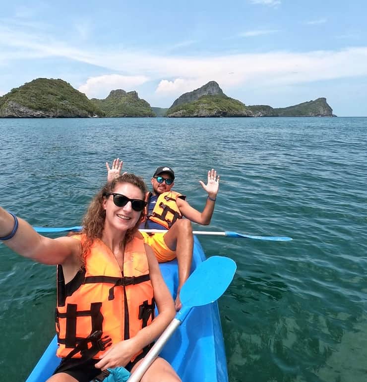A couple ocean kayaking with tree-covered limestone islands behind them