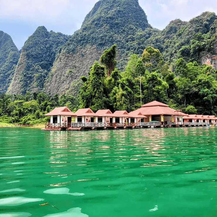 Small bungalows float on the emerald-green Cheow Lan lake, backed by rocky limestone cliffs covered in forest.