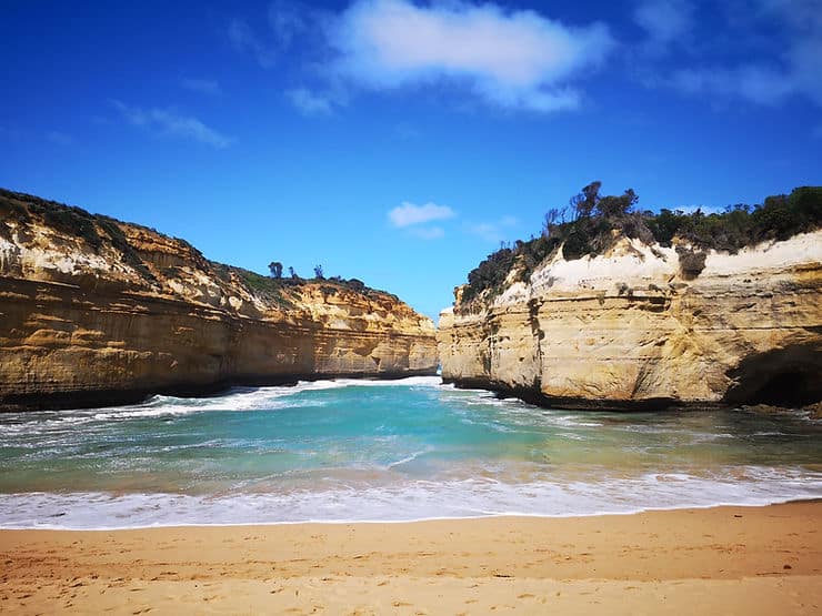 Standing on the sandy beach at Loch Ard Gorge along the Great Ocean Road, surrounded by golden cliffs, creating a secluded cove
