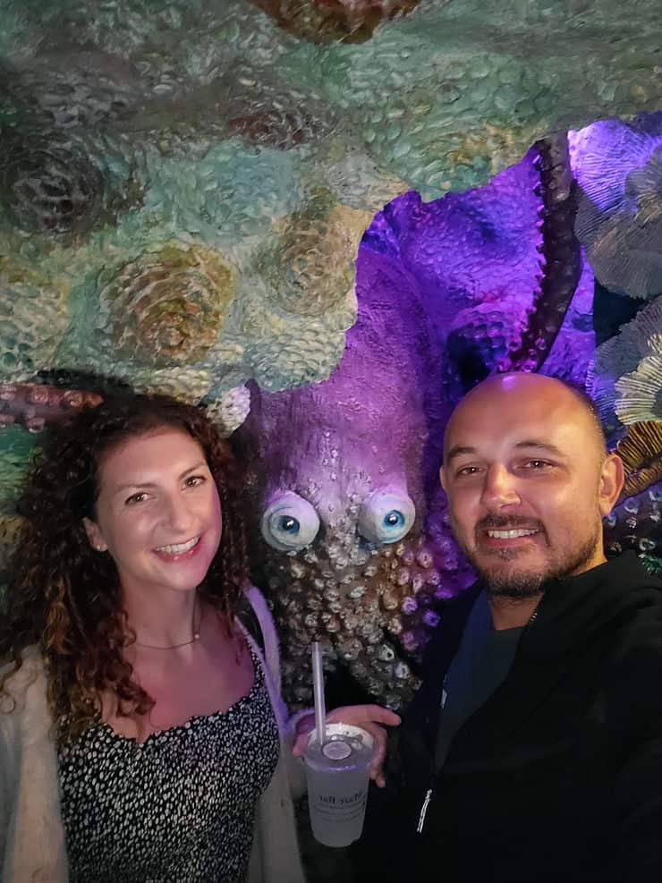 A woman and man stand in front of a fake rock wall with an octopus