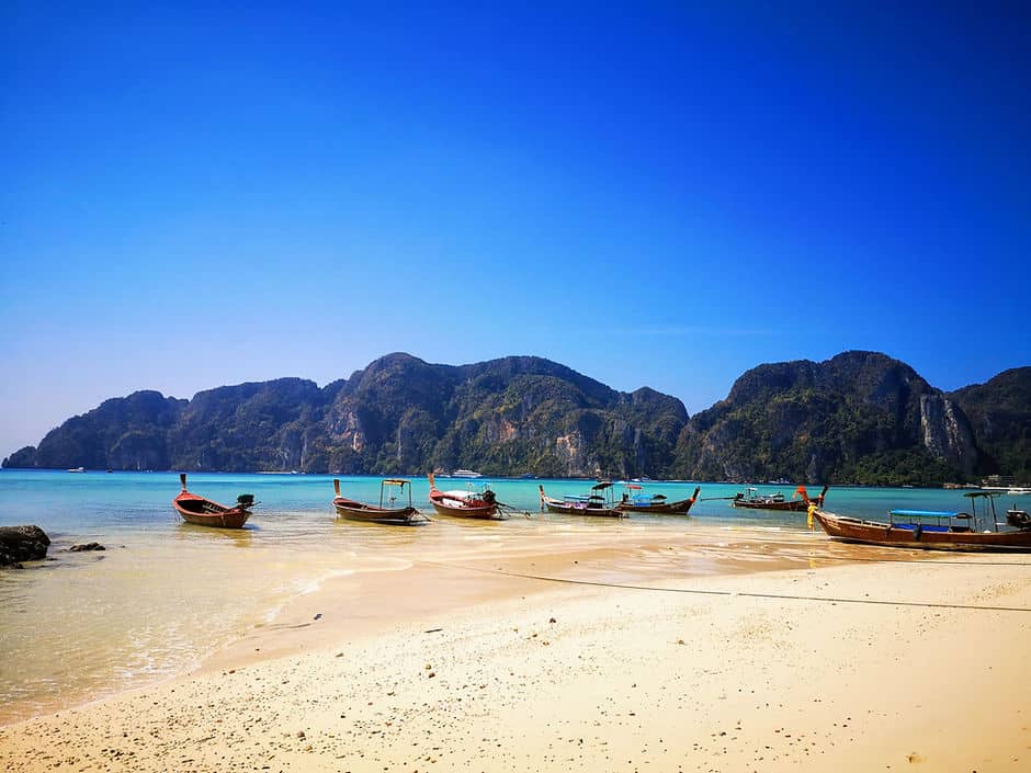 Long tail boats float on the turquoise sea, surrounded by tree covered limestone mountains in Koh Phi Phi, Thailand