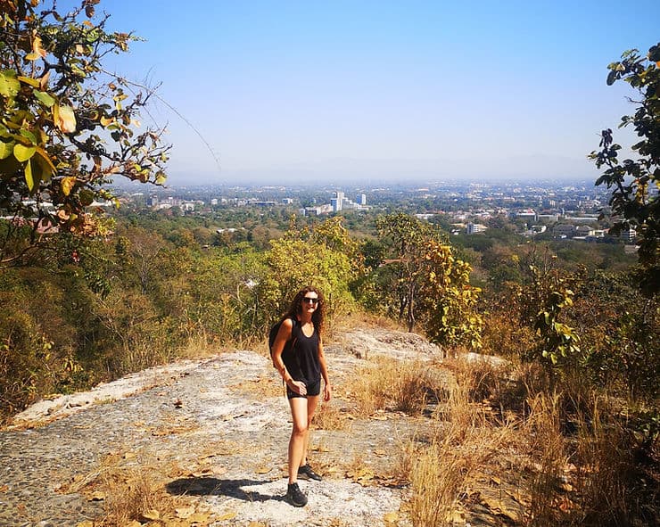 Woman on hiking trail at Huay Kaew waterfall, overlooking the city skyline of Chiang Mai, surrounded by trees.