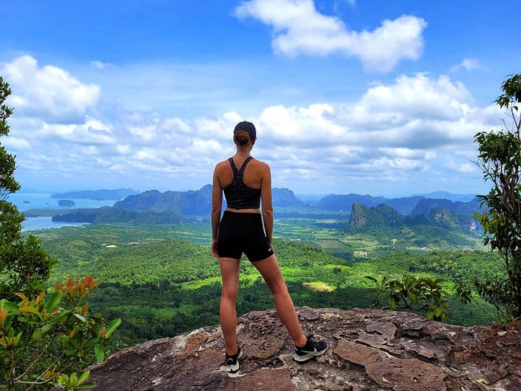 Women standing on the edge of a mountain looking down to thick green forests, backed by limestone mountains and leading to the sea. Dragon Crest hike, Krabi, Thailand