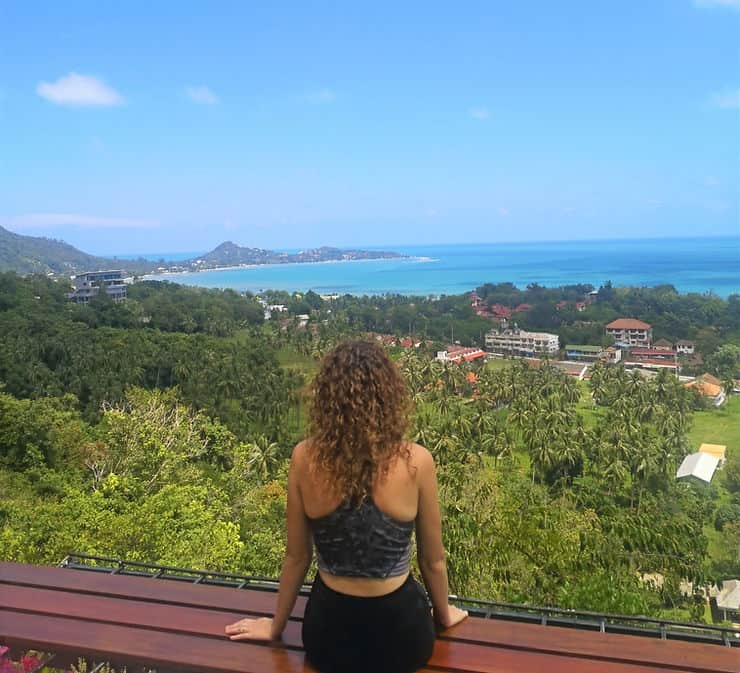 Girl sitting on edge of viewpoint overlooking Koh Samui coastline and mountains