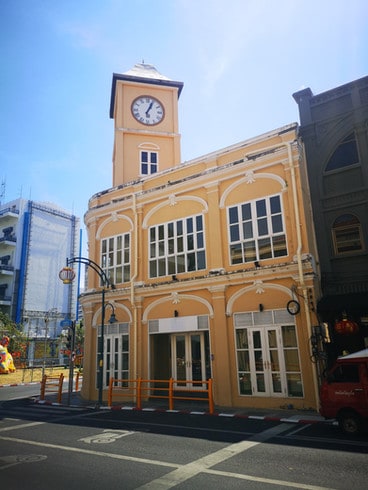A mustard yellow colonial style mansion sits on the corner of the street in Phuket Town, with a small clock tower on the roof
