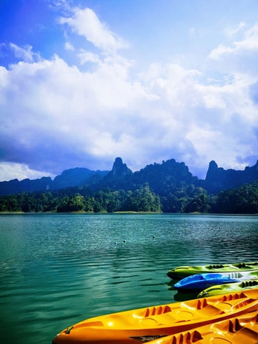 Kayaks are tied up at the raft house. In the background, the calm water of Cheow Lan lake is surrounded by thick forest