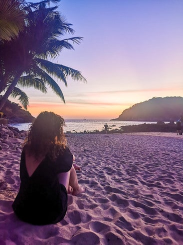 Sitting on the sandy Yanui beach as the sun sets over the sea, creating an orange-purple glow