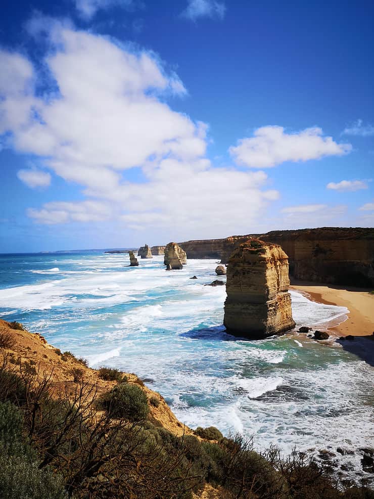 The Twelve Apostles along the Great Ocean Road, sandy rock formations stand high above the shallow water, dotted along the coastline like columns. 