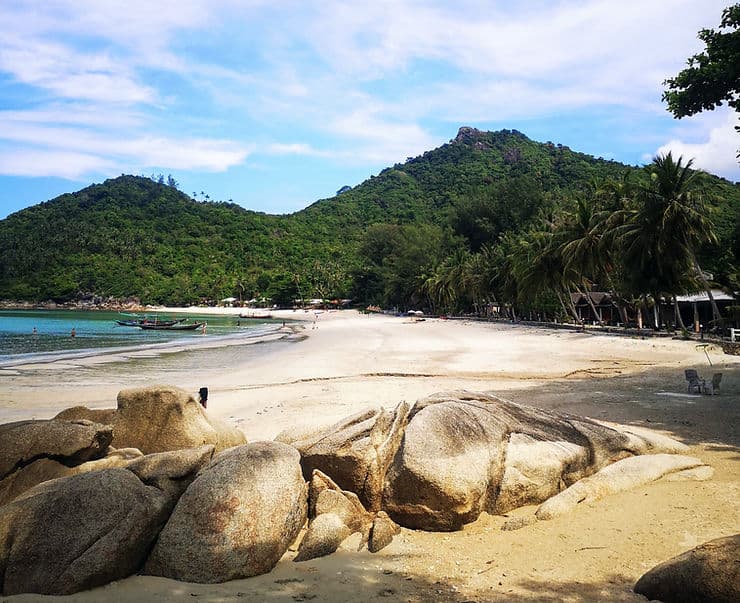 The sandy, secluded Bottle Beach in Koh Phangan, Thailand, backed by palm trees and small huts
