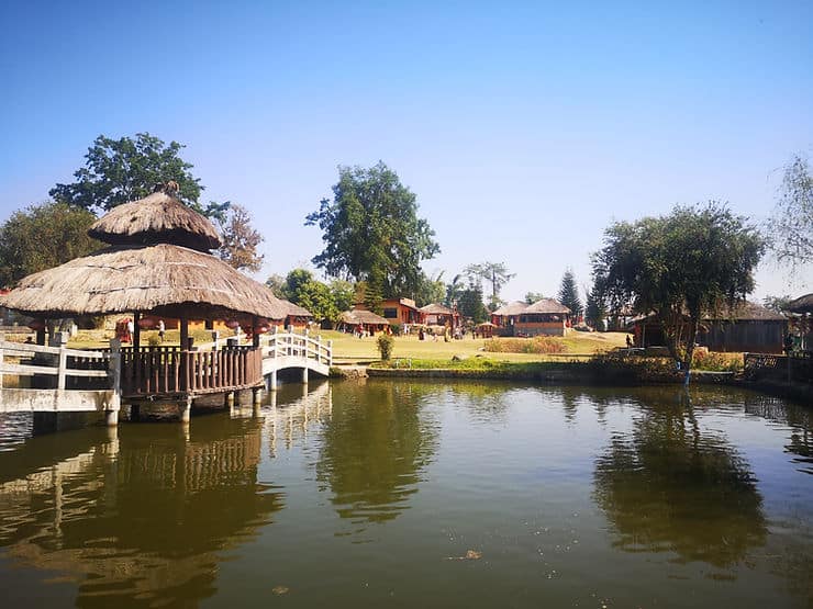 A small bridge with a thatched roof sits over a lake, surrounded by Chinese style huts in Santichon Village, near Pai, Thailand