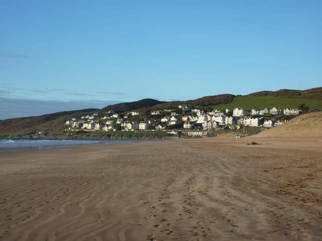 The dark sandy beach of Woolacombe, Devon. With rows of houses perched on the cliffside in the background.