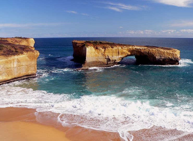 London Bridge viewpoint on the Great Ocean Road - a golden rock formation stands near the sandy shoreline, with a wide arch underneath