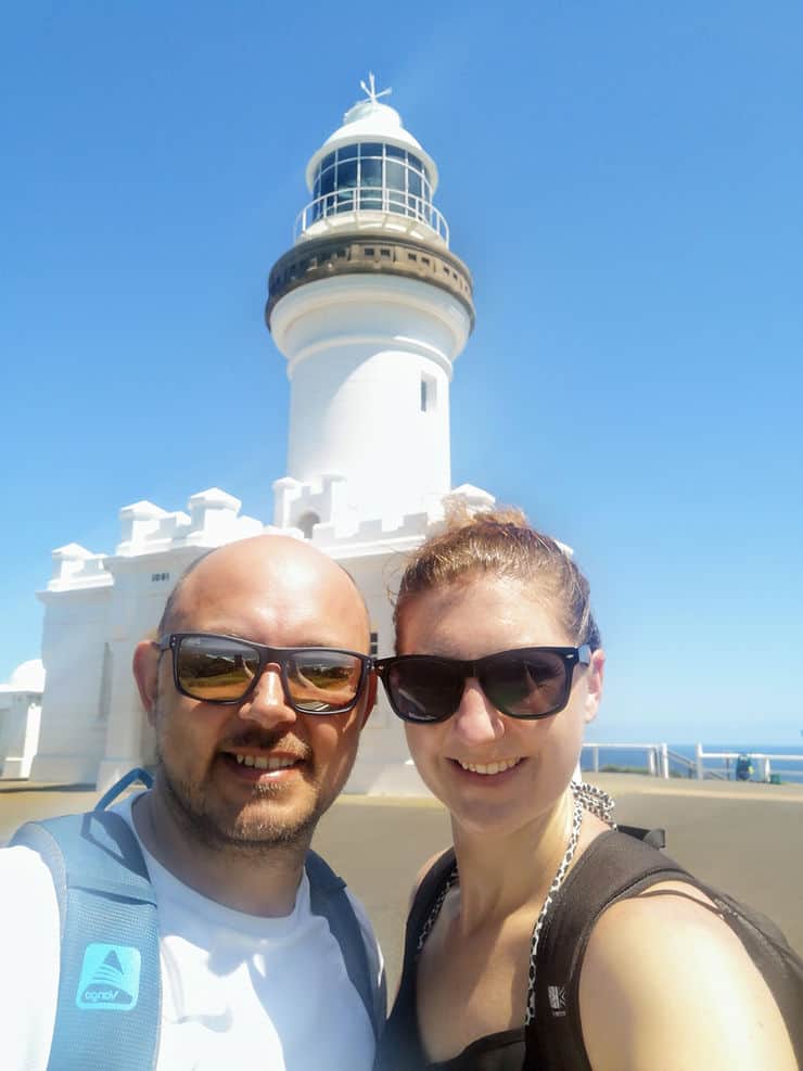 Standing in front of the Cape Byron lighthouse, which is bright white against the blue sky. 