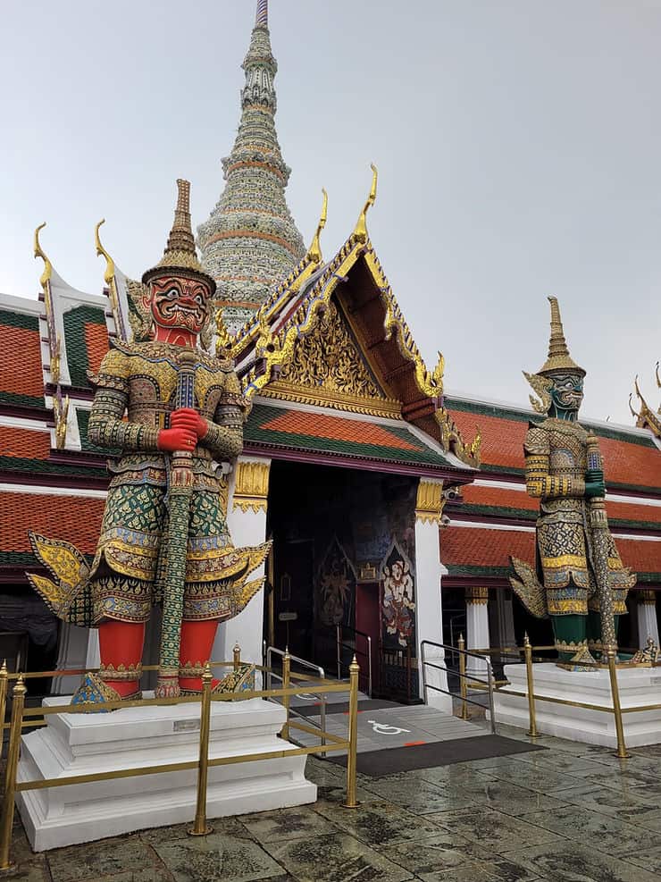 A pair of colourful, embellished statues of Demon Guardians stand tall either side of an entrance into the temple complex within Bangkok's Grand Palace