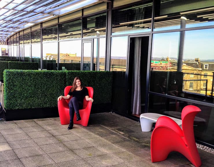 A women sits on a red armchair on a hotel balcony.