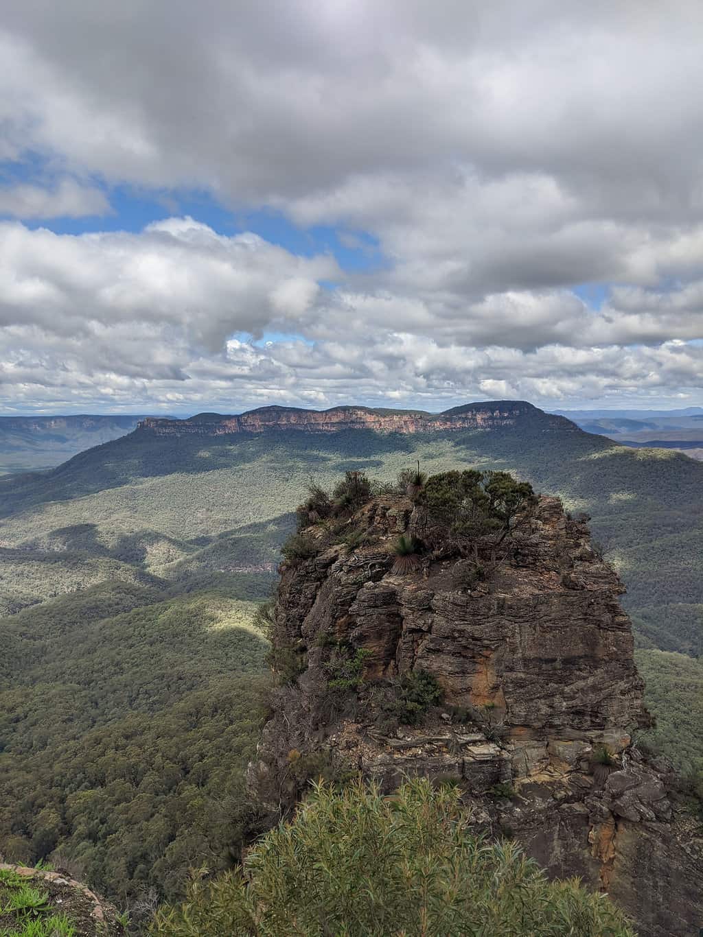 One of the Three Sisters rocks in the foreground, with the valley and mountain range in the background, in the Blue Mountains National Park