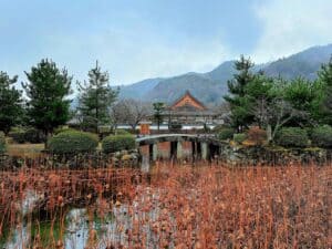 A modest temple with terracotta pitched roof stands above a small pond in Kyoto