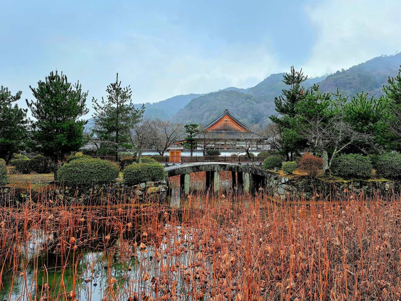 A modest temple with terracotta pitched roof stands above a small pond in Kyoto