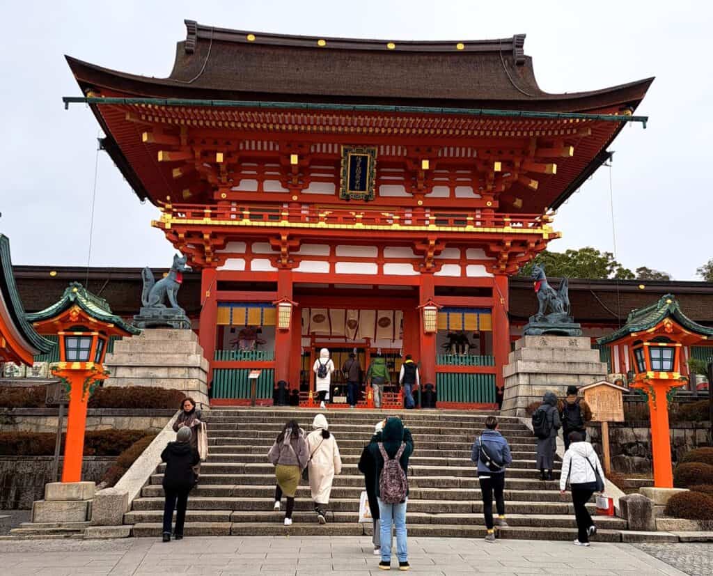 The main hall of Kyoto's Fushimi Inari Shrine is painted red with bright yellow lanterns hanging from the traditional roof.