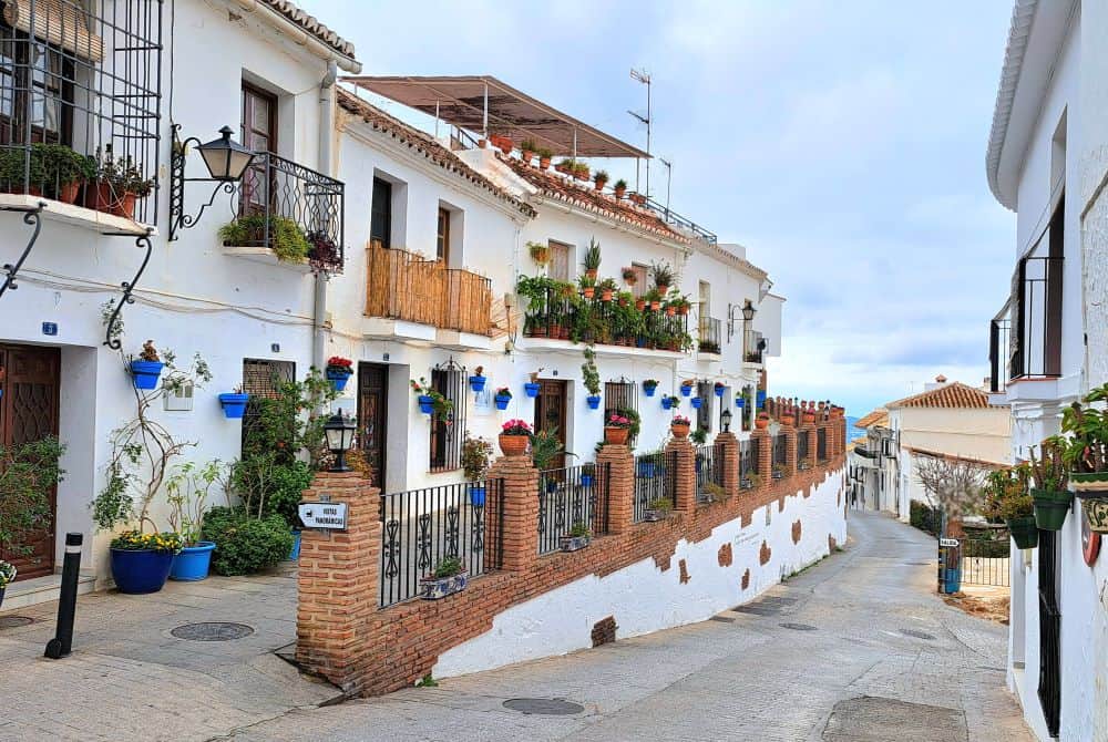 A row of white washed two storey houses adored in blue plant pots and red flowers in the charming Spanish town of Mijas Pueblo.