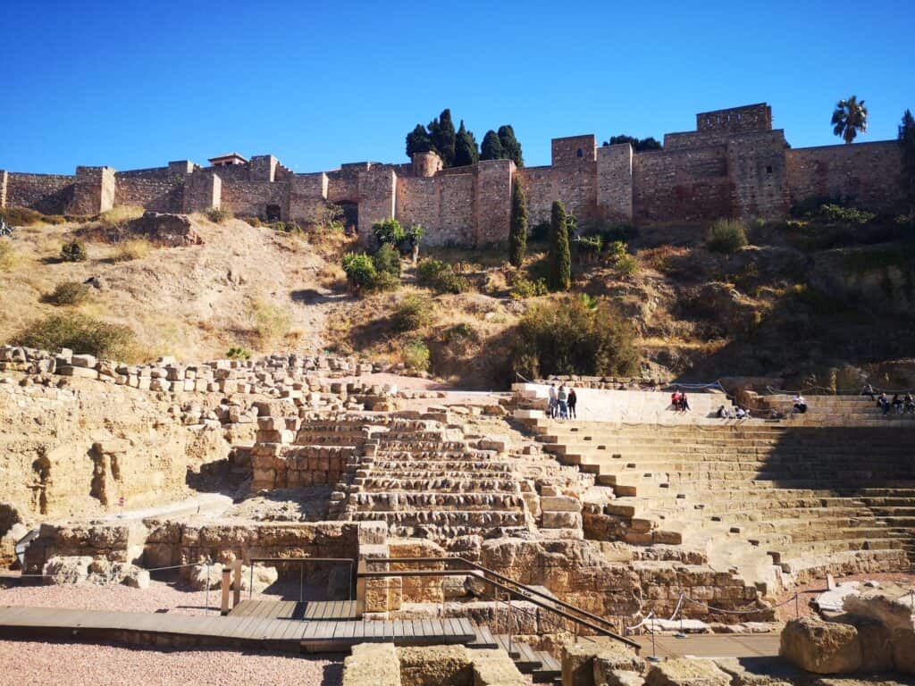 The ruins of a roman ampitheatre sits in front of a large stone wall of the Malaga Alcazaba fortress, which sits on a small hill overlooking the old town.