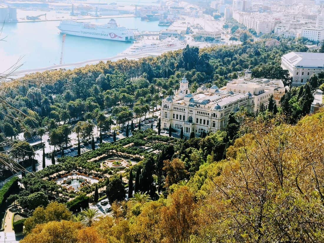 Looking down onto the tree tops of Malaga Park, with the impressive town hall building in the centre. The Port of Malaga can be seen in the background.