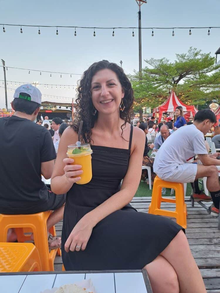 A woman holds a mango smoothie, smiling