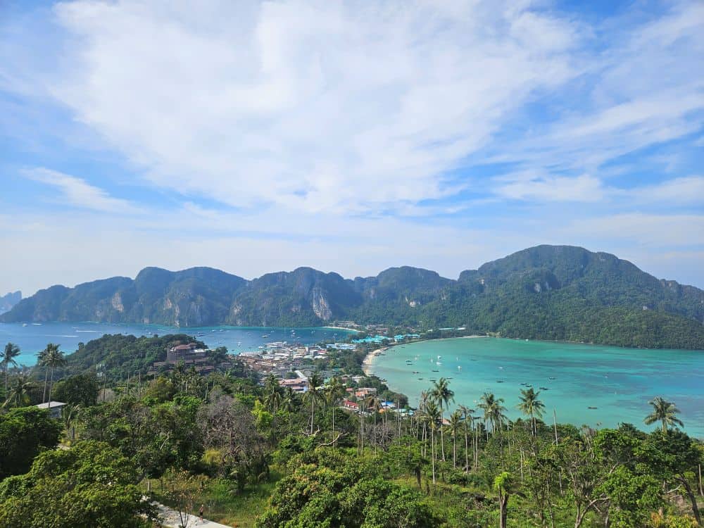 Looking down onto two tree covered islands. The islands are connected by a thin strip of lands with buildings and a thin stretch of white sandy beach.