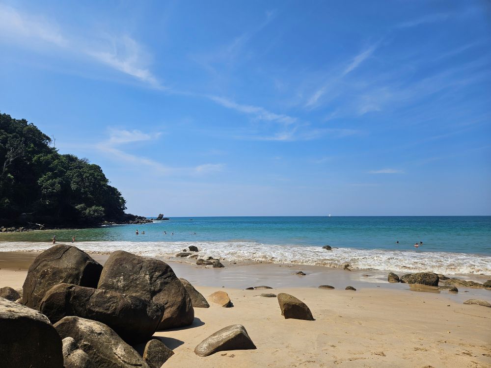 a Cluster of rocks sit on a golden sandy beach. Wave gently lap the shore.